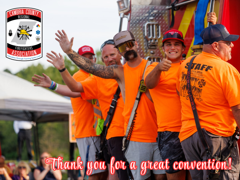 Five smiling men in bright orange shirts stand in a line outside, waving and giving thumbs up, in front of a fire truck. A Cambria County firefighters association logo and thank you message appear on the image.